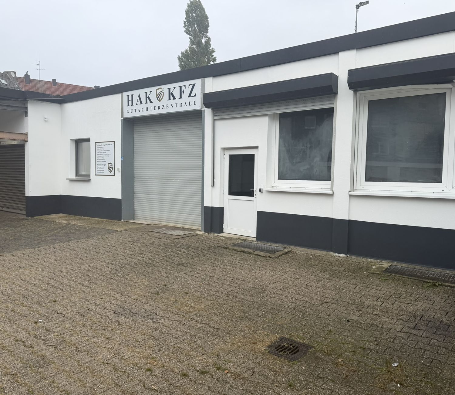 Seitenansicht der HAK KFZ Gutachterzentrale mit Hallentor, Büro und gepflastertem Hof